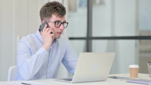 Young Adult Talking on Phone while using Laptop