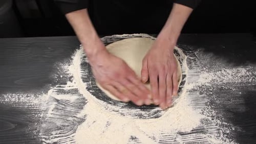 Hands Kneading Dough on Black Surface with Flour