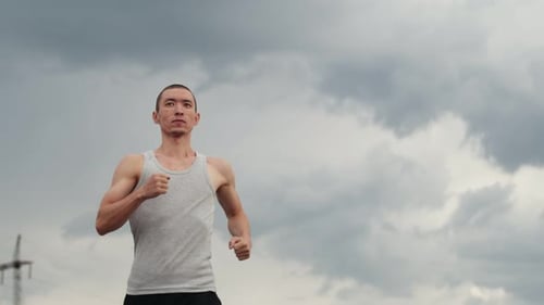 Confident Runner of Athletic Build in Tshirt Runs Along Road Against Background of Overcast Sky