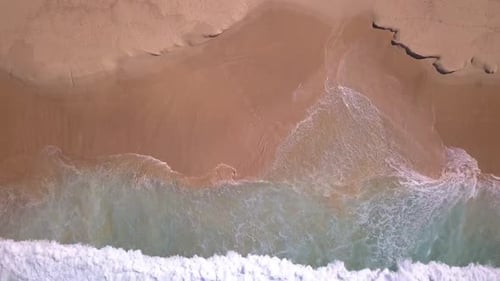 Top aerial view of tropical beach with turquoise ocean water and sea waves reaching shore.