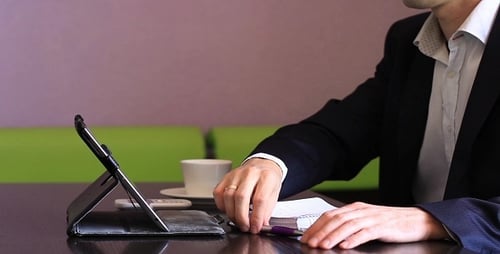 Adult Works On Tablet and Writes in Notebook