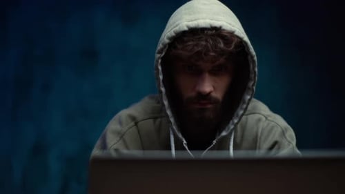 Close-up Portrait of Hacker in Hood Working on Laptop in Dark Room, Tracking Shot in Slow Motion.