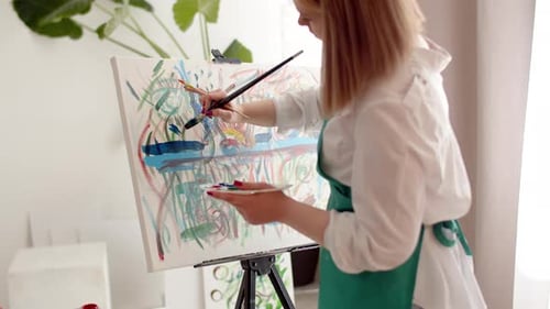 Woman Artist in Studio Paints Multicolored Abstract Painting on Canvas with Brush Back View