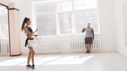 In a Bright Gym with Large Windows a Young Female Athlete Jumps on a Rope Under the Supervision of a