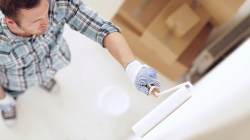 Man malt Wand mit Walze und weißer Farbe