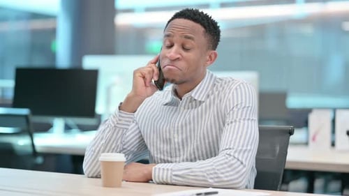 African Businessman with Coffee Talking on Smartphone in Office