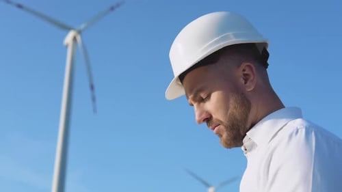 Retrato de un hombre con un casco blanco y una camisa clásica sobre el fondo de una turbina eólica de un