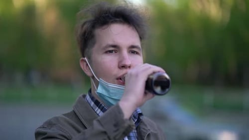 Guy Takes Off Medical Protective Face Mask and Drinks Lemonade From a Glass Bottle