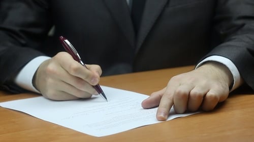 Man Signing Document on Wooden Desk Close Up