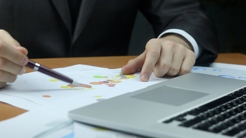 Businessman Reviews Charts and Types on Laptop