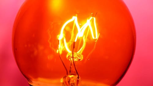 Illuminated Lightbulb Filament Against Red Background Close-up