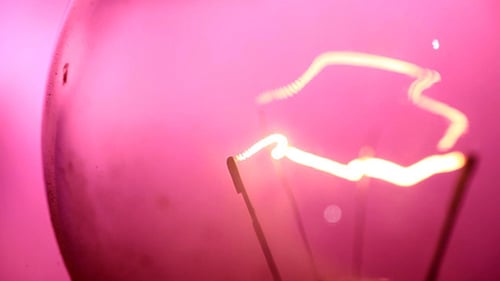 Glowing Light Bulb Filament against Pink Background