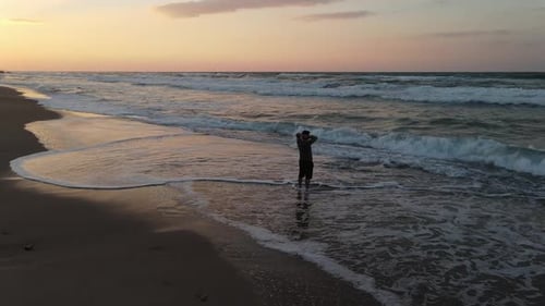 Man Standing in Surf on Beach at Sunset