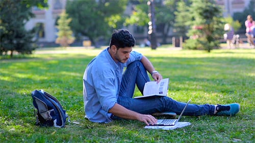 Young Adult Studying on Park Lawn with Laptop