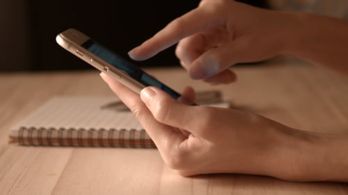 Adult Using a Smartphone on a Wooden Desk