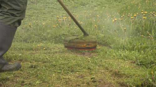 Man Trimming Green Grass Field with String Trimmer