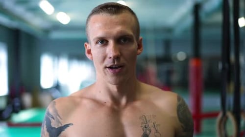 Confident Tattooed Young Sportsman Looking at Camera Breathing Heavily Standing in Gym Indoors