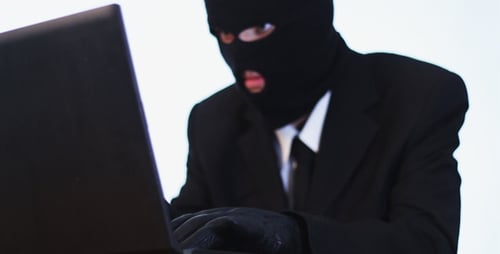 Balaclava Wearing Individual Typing on a Laptop