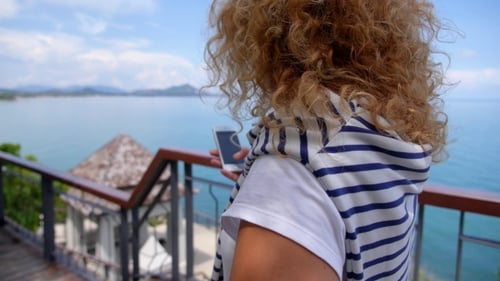 Woman Uses Phone Overlooking Tropical Ocean View