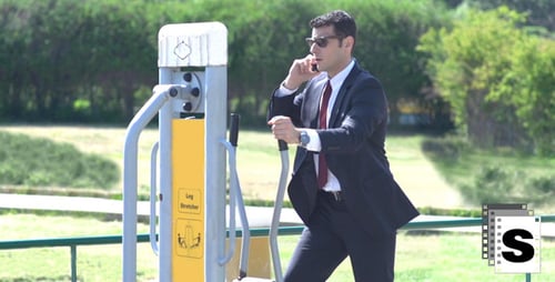 Businessman Exercising on Leg Stretching Machine While on Phone