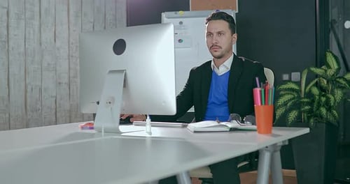 Businessman in Glasses Sits at Computer in Office