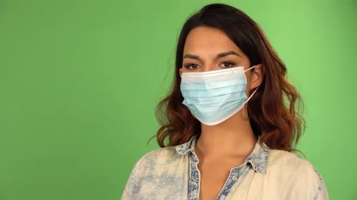 A Caucasian Woman Puts on a Face Mask Looks at the Camera Takes the Mask Off Green Screen