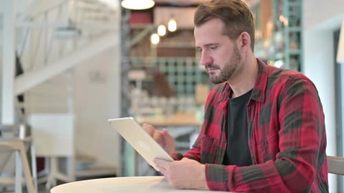Serious Young Man Using Digital Tablet in Cafe
