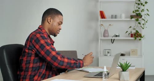 Busy African American Guy Student Doing Homework for University at Home Using Laptop and Notebook