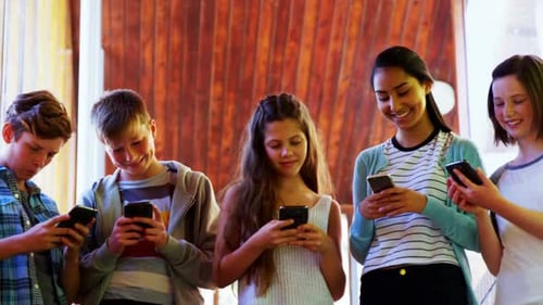 Group of smiling school friends using mobile phone in corridor