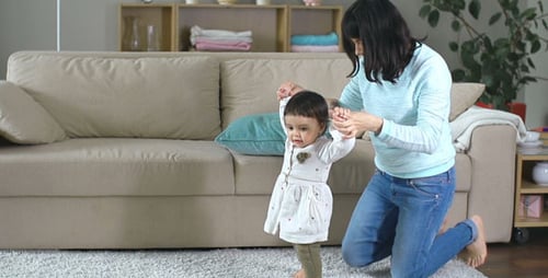 Woman Helping Adorable Infant Learning To Walk At Home