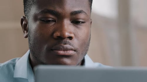 Ernsthafter männlicher junger afroamerikanischer Geschäftsmann Programmierer tippt am Computer im Home Office fokussiert