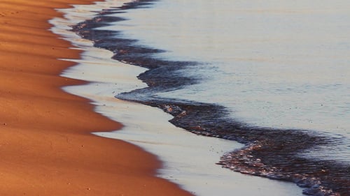 Meereswellen und Sandstrand bei Sonnenaufgang