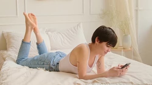 Young Woman Relaxes with Cell Phone on Bed