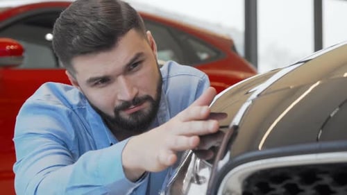 Handsome Man Smiling to the Camera While Examining a New Car at Dealership