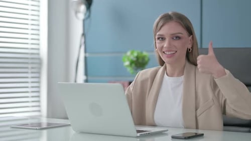 Businesswoman Showing Thumbs Up Sign While Using Laptop in Office