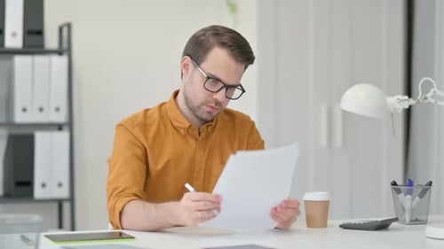 Man Reviews Documents at Desk in Office
