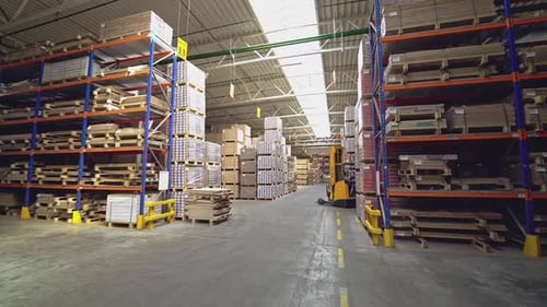 An orange electric stacker is driving between the shelves with goods in stock.