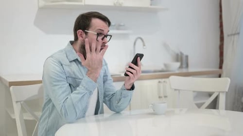 Sad Beard Young Man Facing Loss on Smartphone in Office