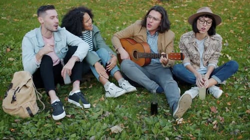 High Angle View of Male and Female Friends Playing the Guitar Singing in Park