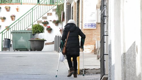 Woman Walking with Crutch on Urban Street