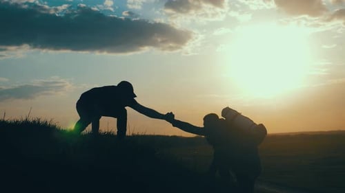 Friends Helping Each Other Hike at Sunset