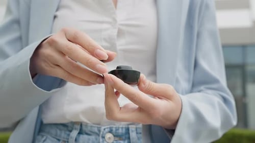 Woman Opens Earbud Case Outside Building