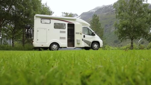 Recreational Vehicle Parked in Green Field with Mountains