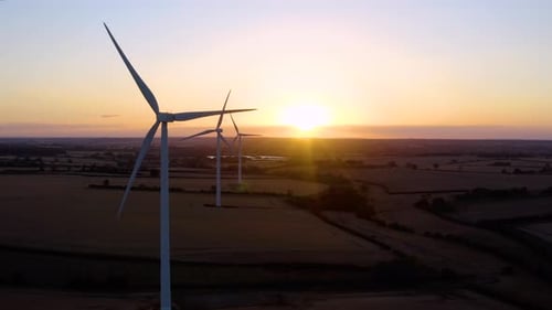 Large wind turbines with blades in field aerial view bright orange sunset.