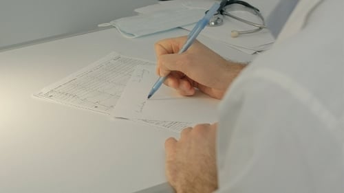 Doctor Writing on Paperwork in Clinic Office