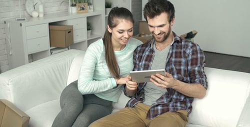 Young Couple Relaxing on Couch with Tablet After Moving