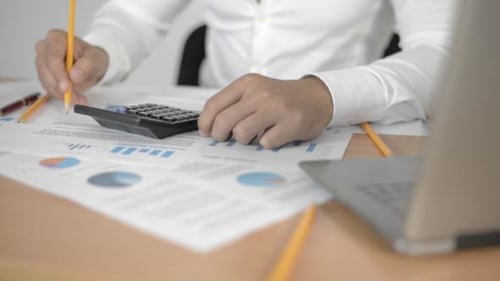 Man Calculates Finances at Desk with Laptop