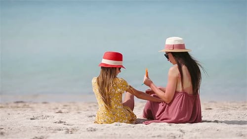 Junge Mutter trägt Sonnencreme auf die Nase der Tochter am Strand auf. Sonnenschutz