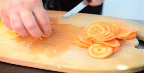Hands Carefully Slicing Carrot on Cutting Board