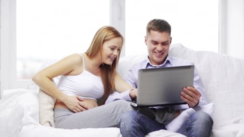 Happy Couple Expecting, Using Laptop on Sofa